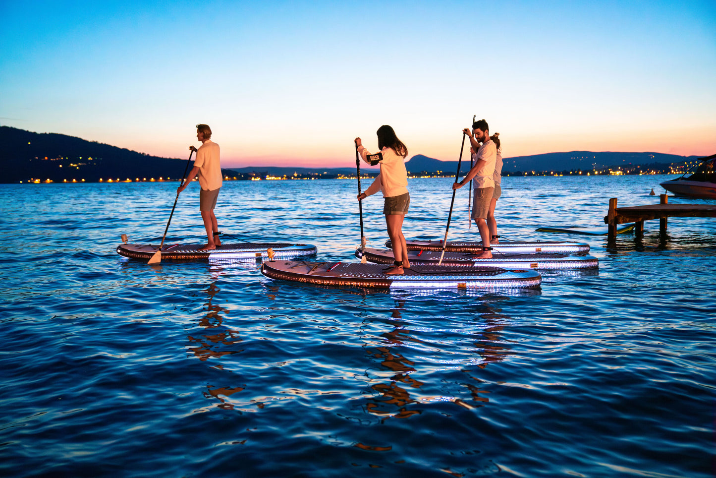 Group of paddleboarders glowing on the lake under moonlight during a night session – book a moonlight paddle party at MontanaBoardingSchool.com. Rent full daily and weekly rates at MTBoarders.com or buy now from eboarders.com