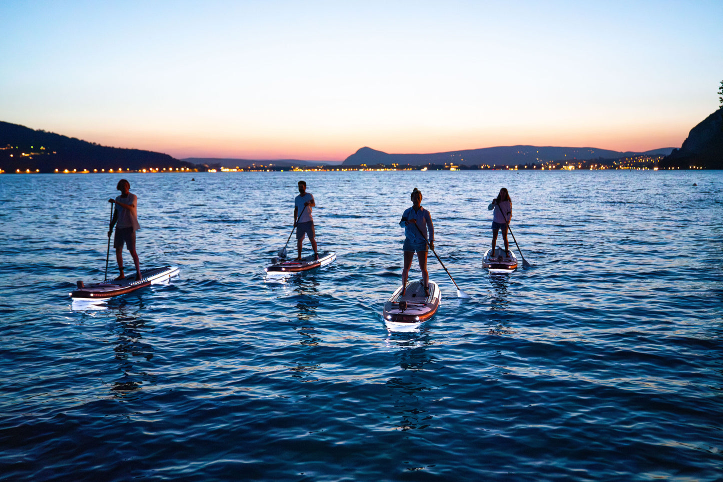 Group of paddleboarders glowing on the lake under moonlight during a night session – book a moonlight paddle party at MontanaBoardingSchool.com. Rent full daily and weekly rates at MTBoarders.com or buy now from eboarders.com
